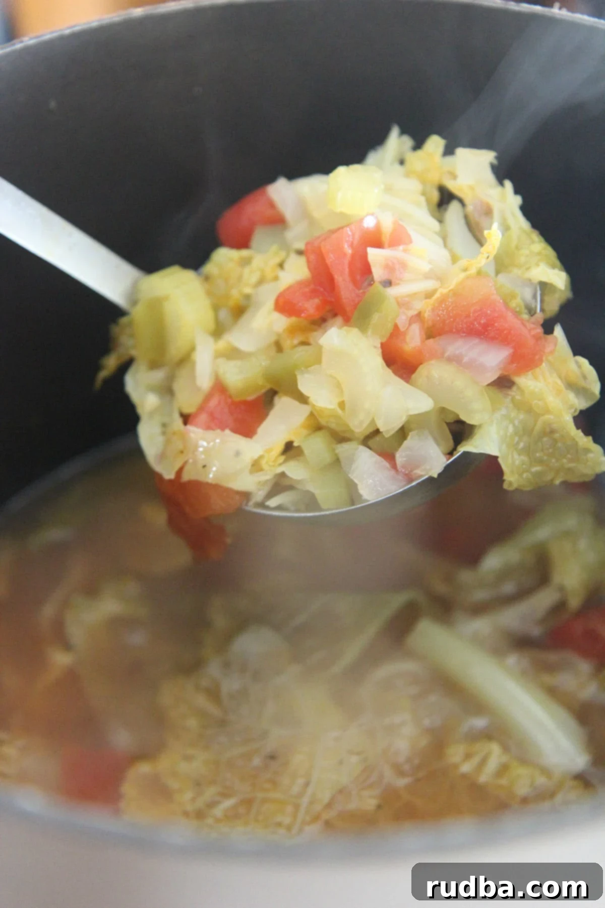 A ladle filled with vibrant, steaming cabbage soup, held over a large pot brimming with more soup. 