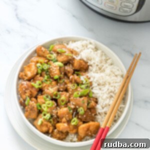 sesame chicken with a side of white rice in a white bowl with chop sticks on top and an instant pot in the background.