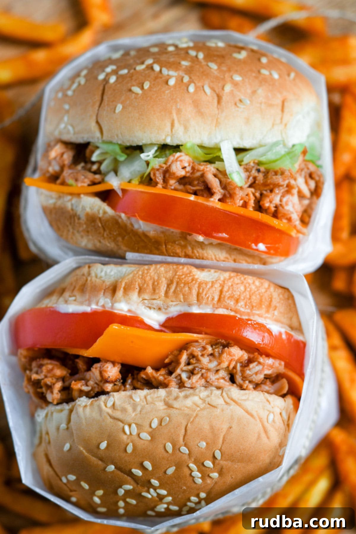 A tantalizing stack of two shredded chicken sandwiches, adorned with fresh toppings, with a tempting bed of sweet potato fries peeking out from underneath.