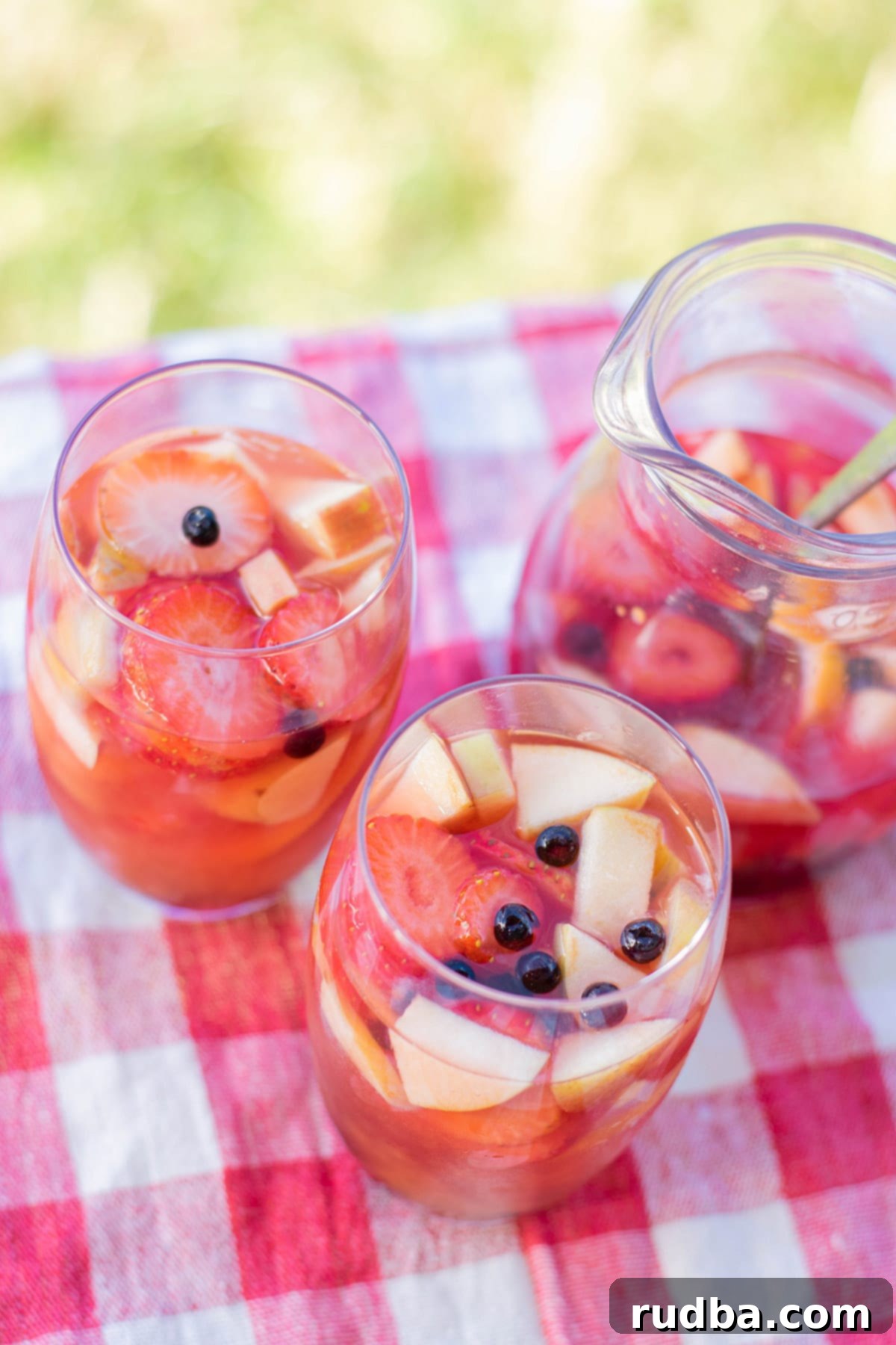 two glasses filled with mango sangria on a picnic table outside. With a pitcher in the background filled with sangria. 