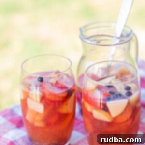 Tropical Mango Sangria 4 two glasses filled with sangria and fruit on top of a red and white table cloth and a pitcher with sangria in the background.