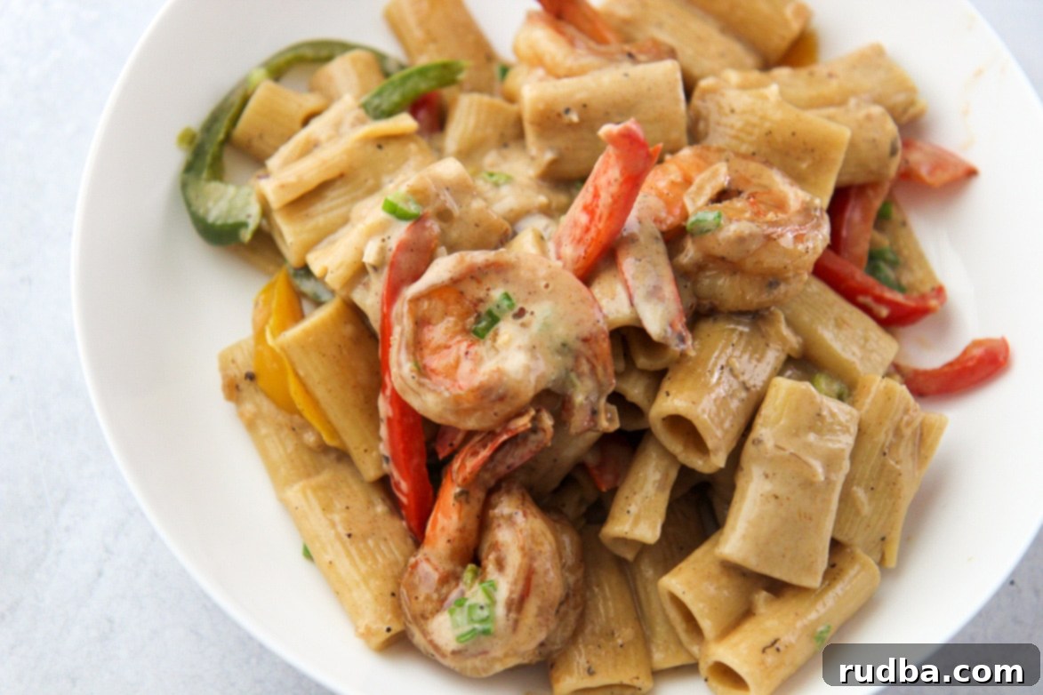 Close-up of Rasta Pasta in a white bowl, showcasing the creamy sauce, colorful peppers, and shrimp.