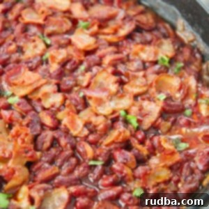 Sweet and Smoky Chipotle Baked Beans 4 Chipotle baked beans in an iron skillet with bacon and parsley on top.