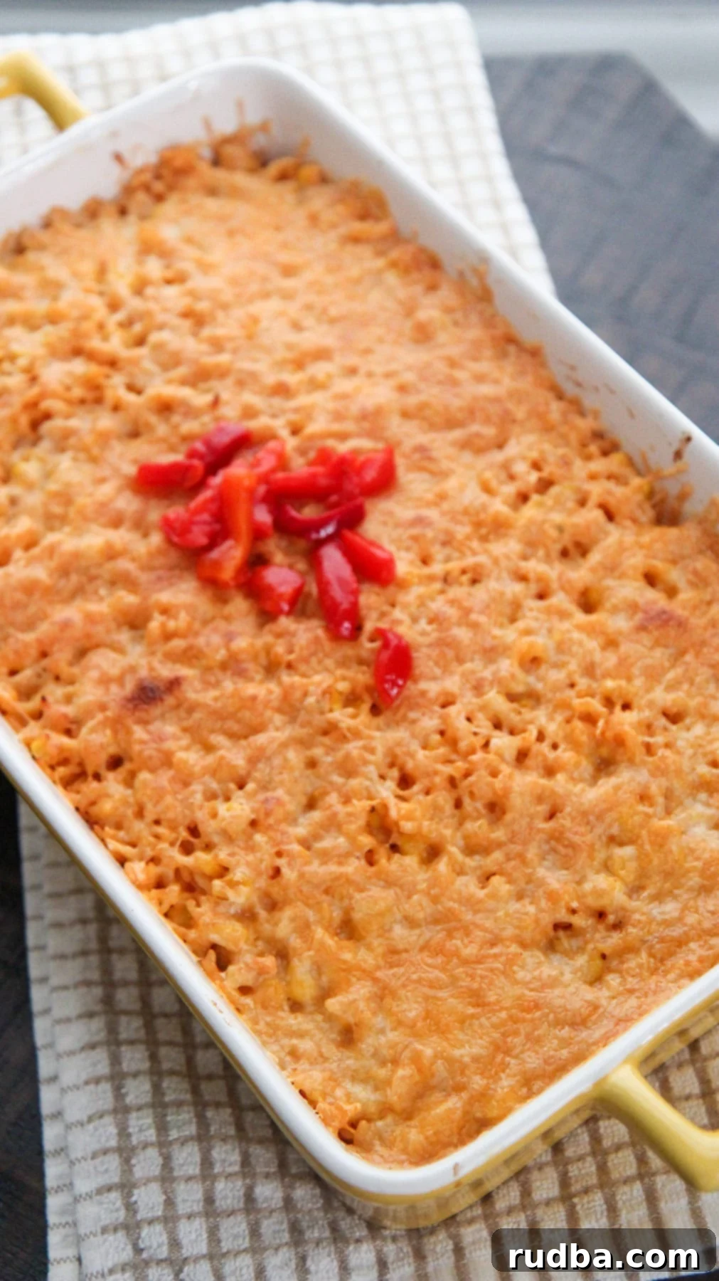 A vibrant Arroz Imperial in a yellow casserole dish, featuring golden melted cheese and decorative red peppers on top.