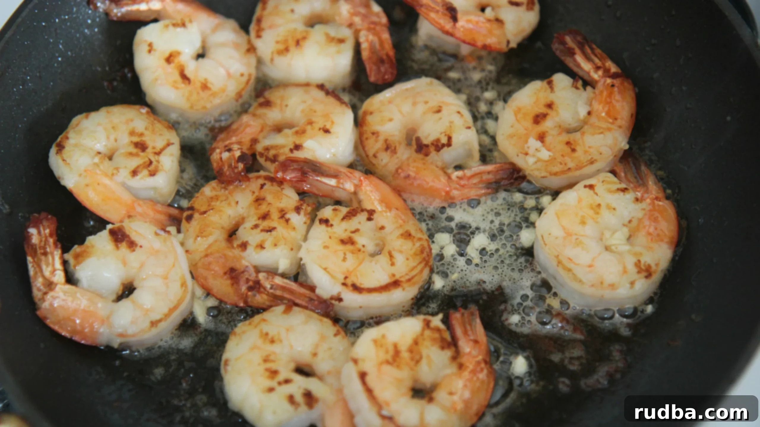 Close-up of perfectly cooked honey garlic shrimp glistening in a black skillet, ready to be served.