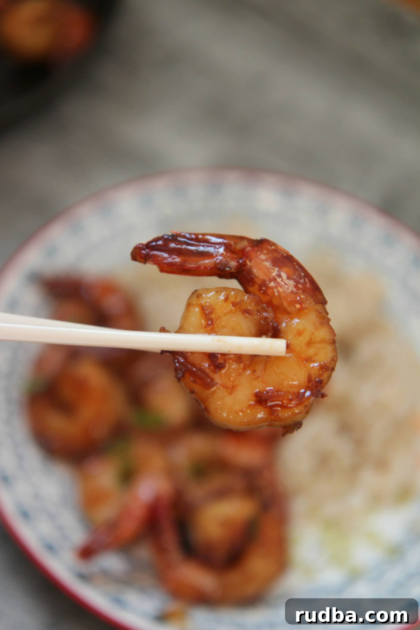 A single piece of honey garlic shrimp held by chopsticks, ready to be enjoyed.