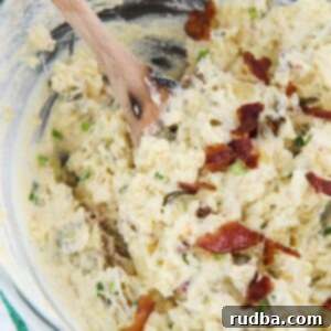 Fiery Spud Salad 4 spicy potato salad in a glass bowl with bacon on top, a wooden spoon, and a green and white towel on the side.