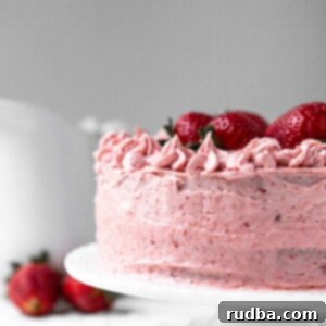 Berry Bliss Cake 6 two layer fresh strawberry cake on a white cake stand with a white pitcher in the background and strawberries on the side.