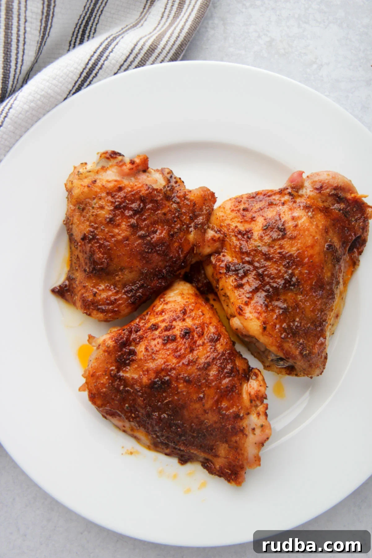 three baked chicken thighs on a white plate with a gray and white towel on the side. 