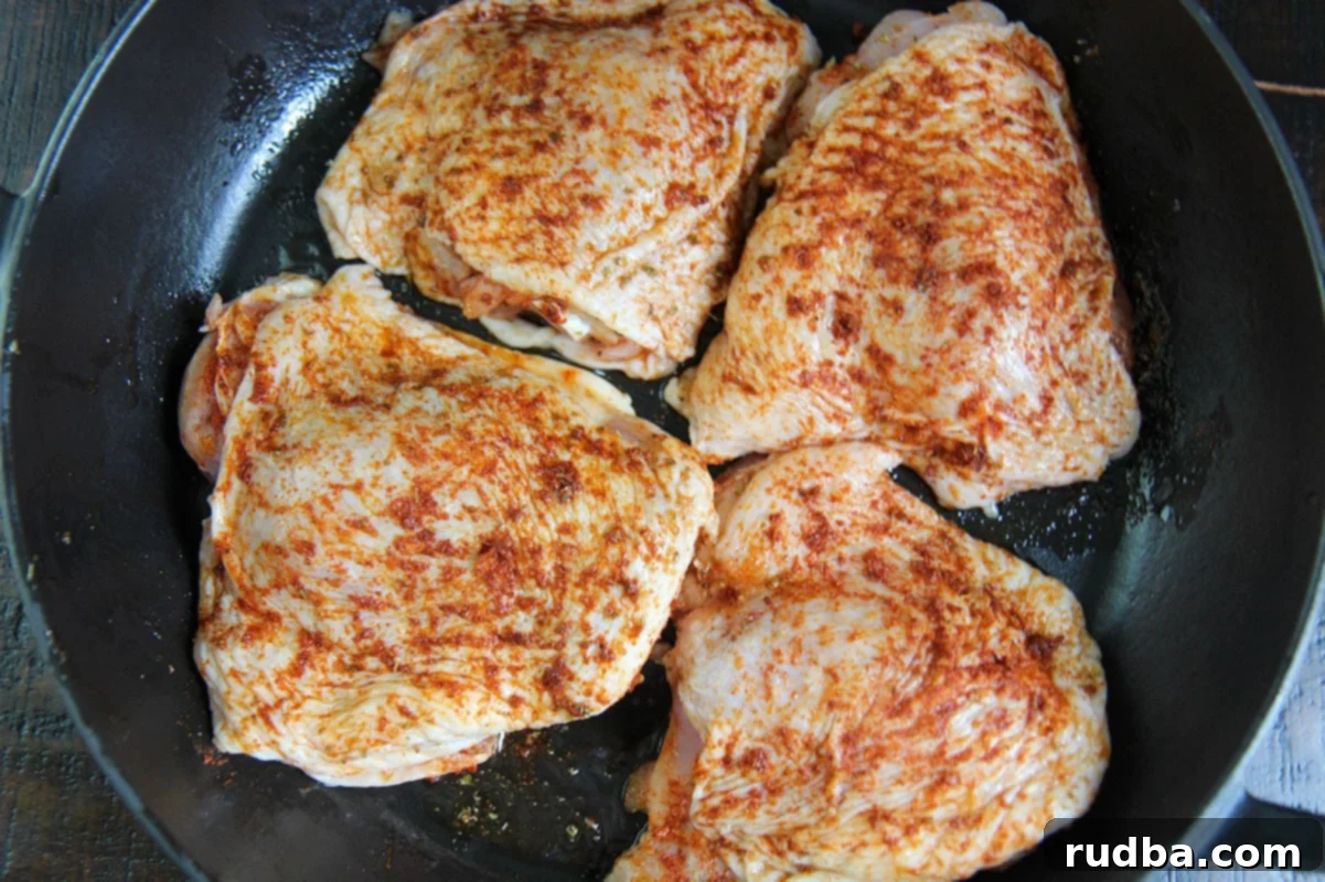 four raw chicken thighs seasoned in a cast iron skillet. 
