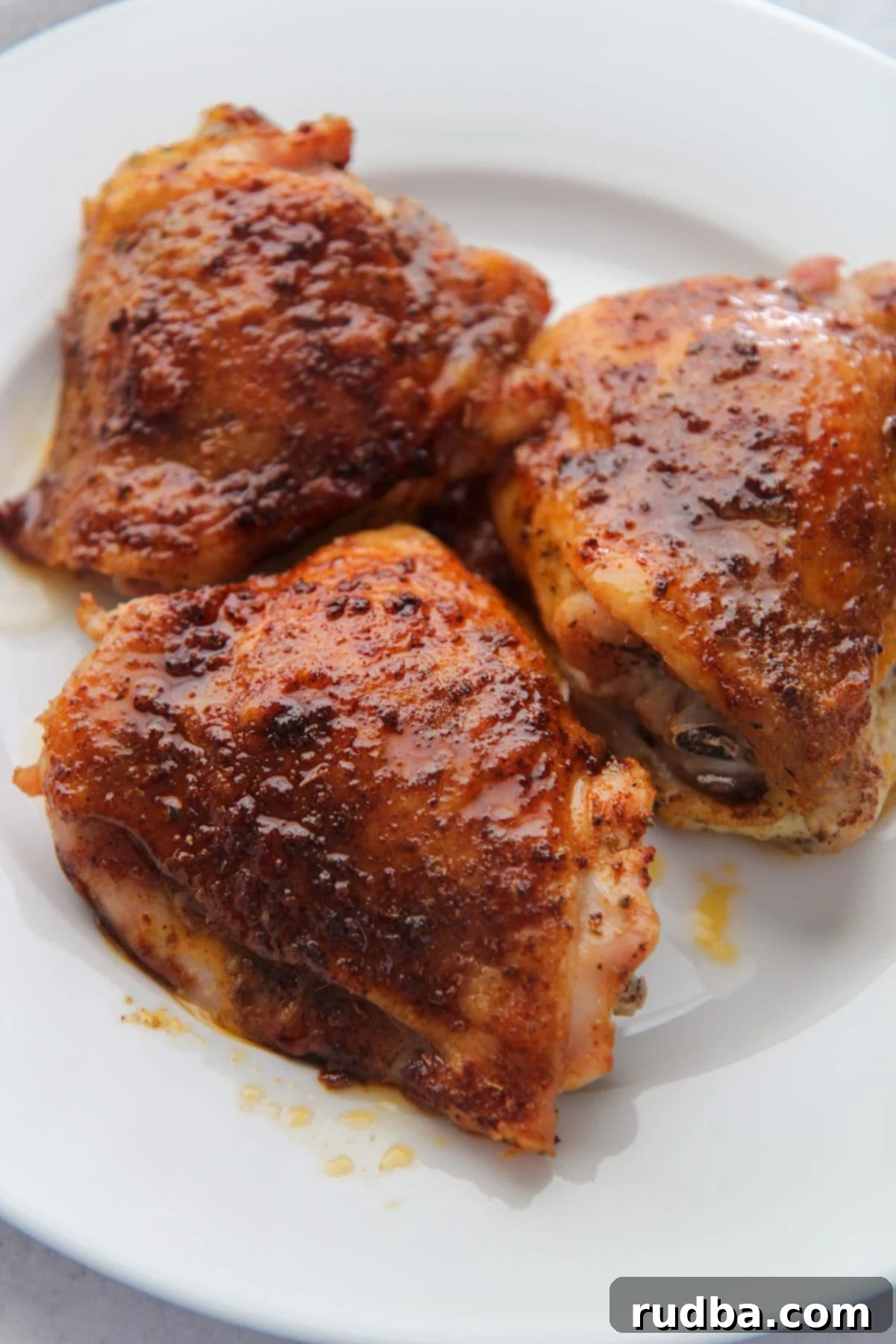 three crispy colorful chicken thighs on a white plate up close. 