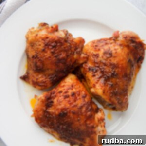 Succulent Oven Roasted Chicken Thighs 5 three baked chicken thighs on a white plate with a gray and white towel on the side.