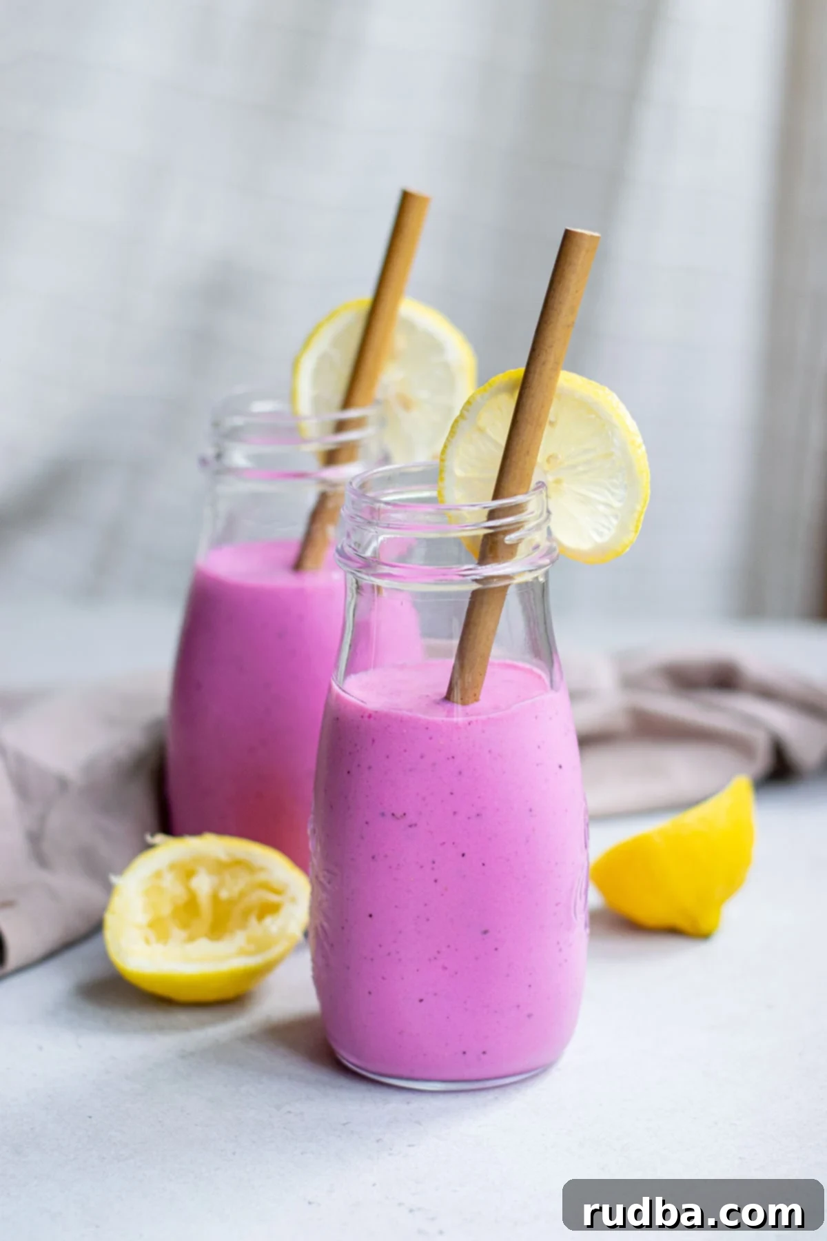 two glass jars filled 3/4s of the way with pink dragon fruit smoothie with lemons and brown straws.