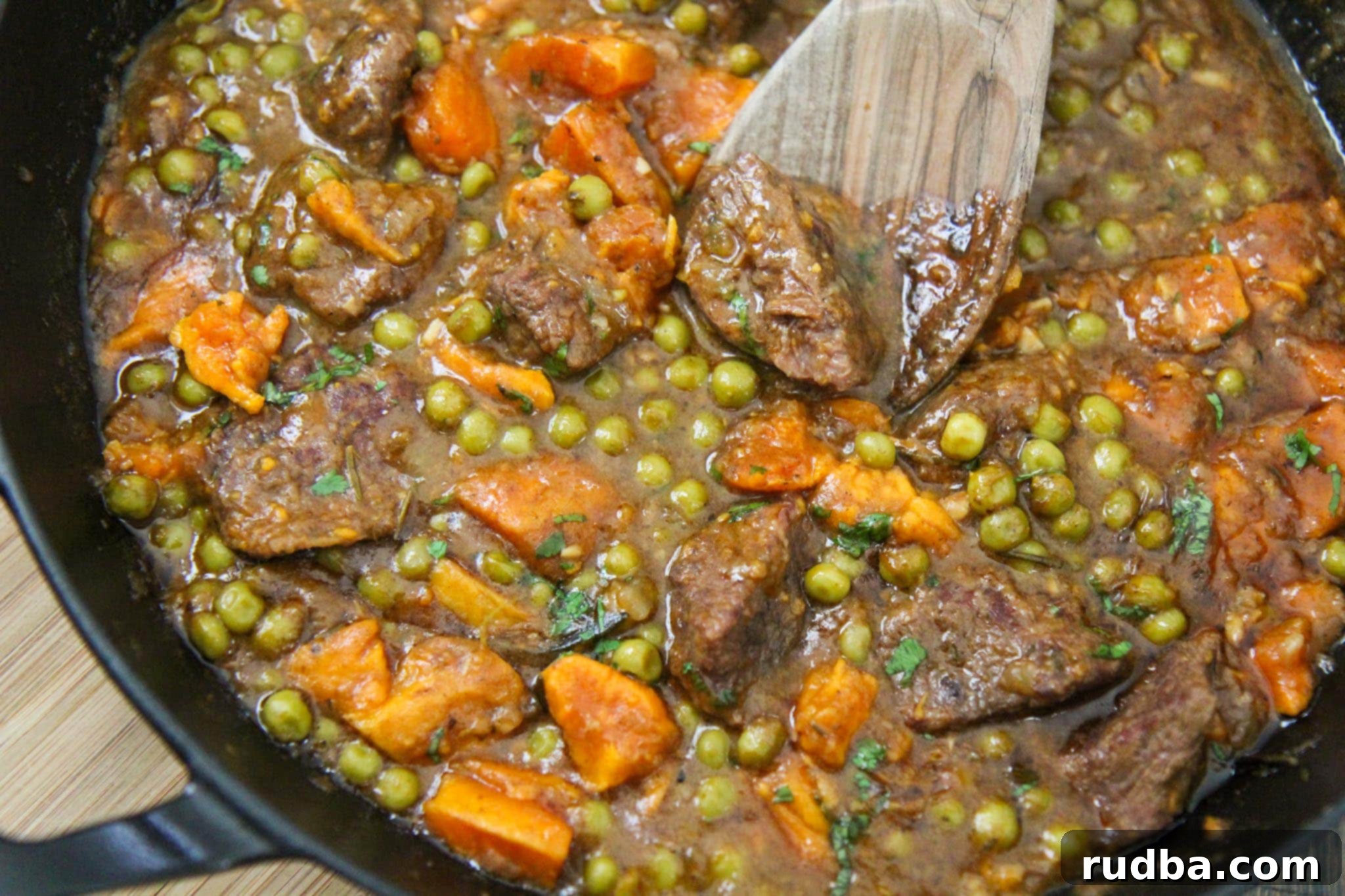 A close-up of a rich and savory beef and sweet potato stew, served in a black skillet, highlighting the tender meat and vibrant vegetables.