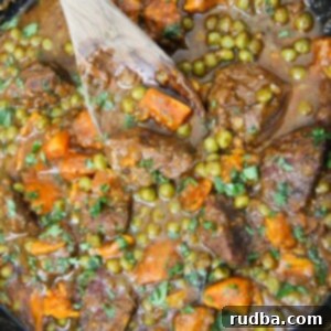 Hearty Beef and Sweet Potato Stew 4 sweet potatoes, green peas, beef cubes, and a wooden spoon in a cast iron skillet.