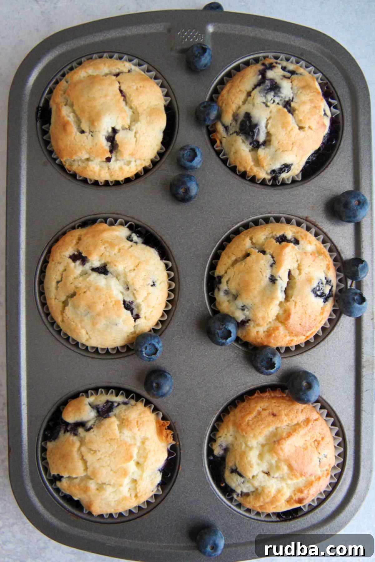 A muffin pan filled with six freshly baked, golden brown blueberry muffins, ready to cool