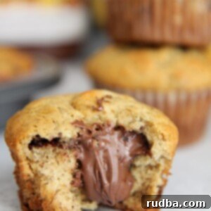 Gooey Nutella-Filled Banana Muffins 5 Nutella stuffed banana muffin up close with a nutella jar and more muffins in the background.