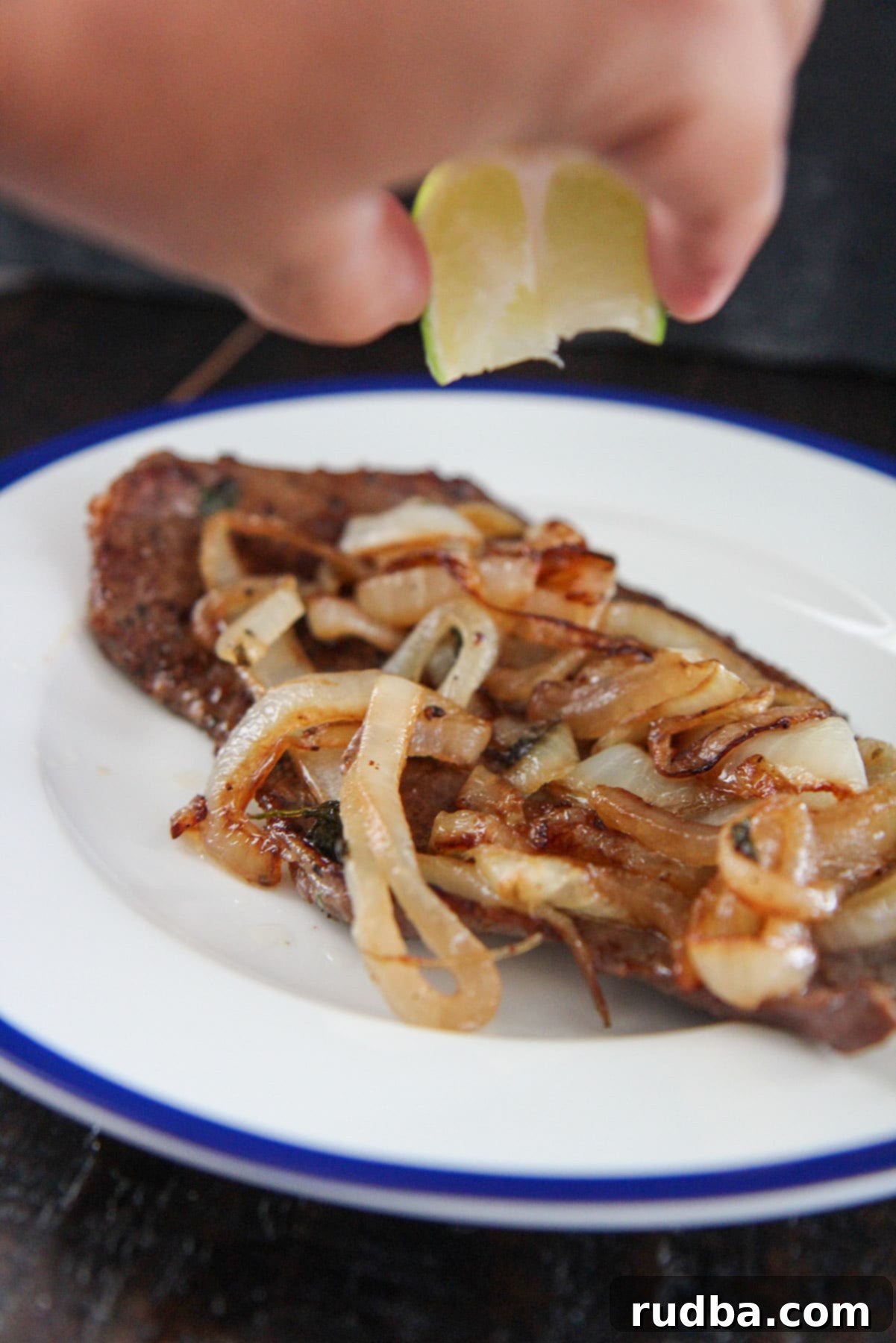 bistec encebollado with a hand squeezing lime juice over it. 