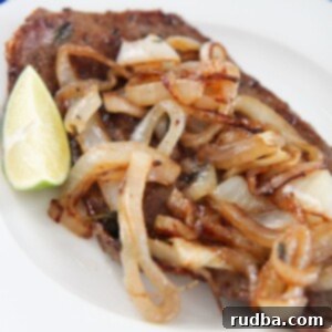 Cuban style steak and onions on a white plate with a lime wedge on the side.