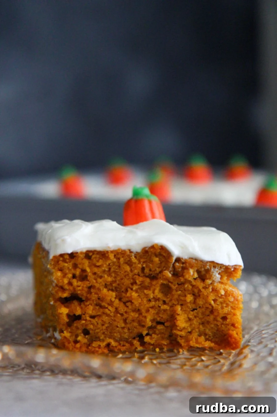 A close-up slice of moist pumpkin cake generously topped with homemade cream cheese frosting.