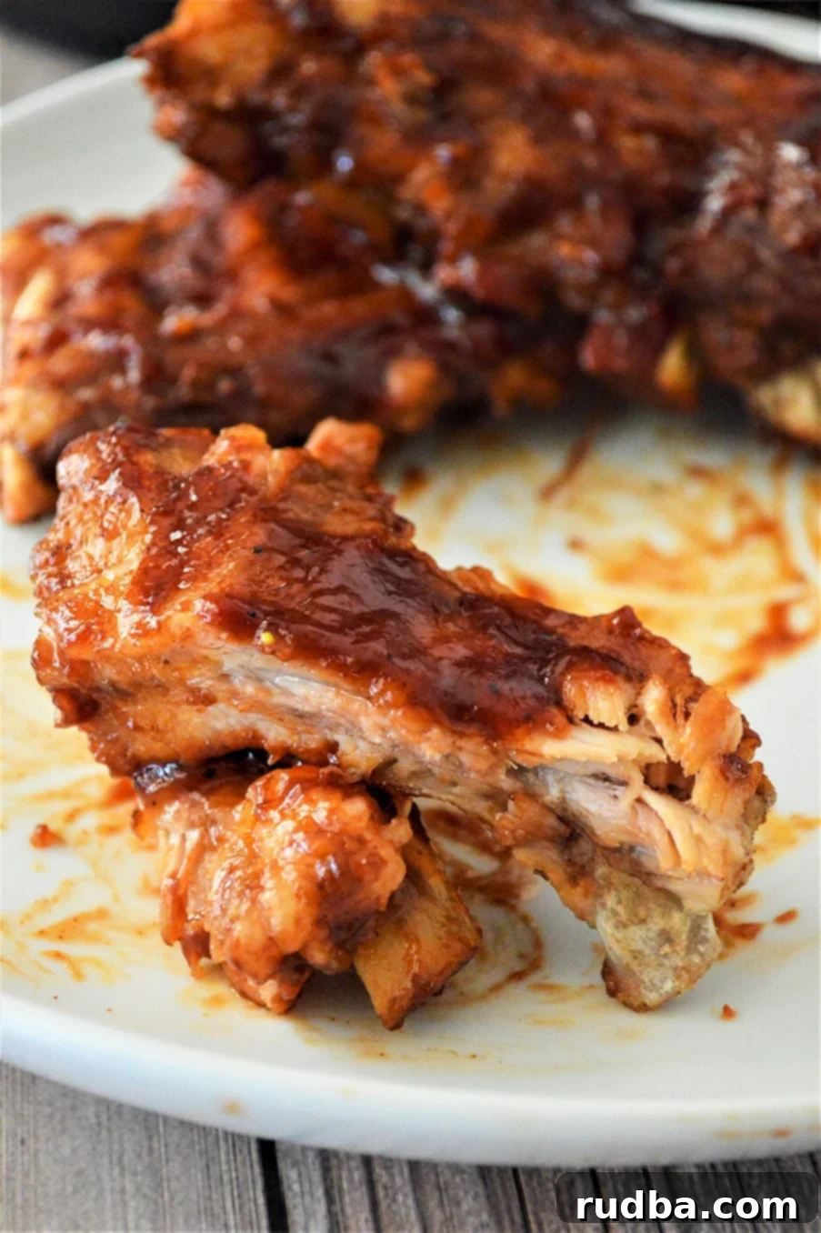 Close-up of perfectly barbecued ribs on a pristine white plate, showcasing the rich sauce and tender meat.