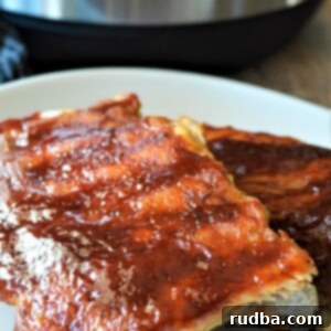 Two racks of BBQ ribs on a white plate up close, showcasing a rich, caramelized barbecue sauce.
