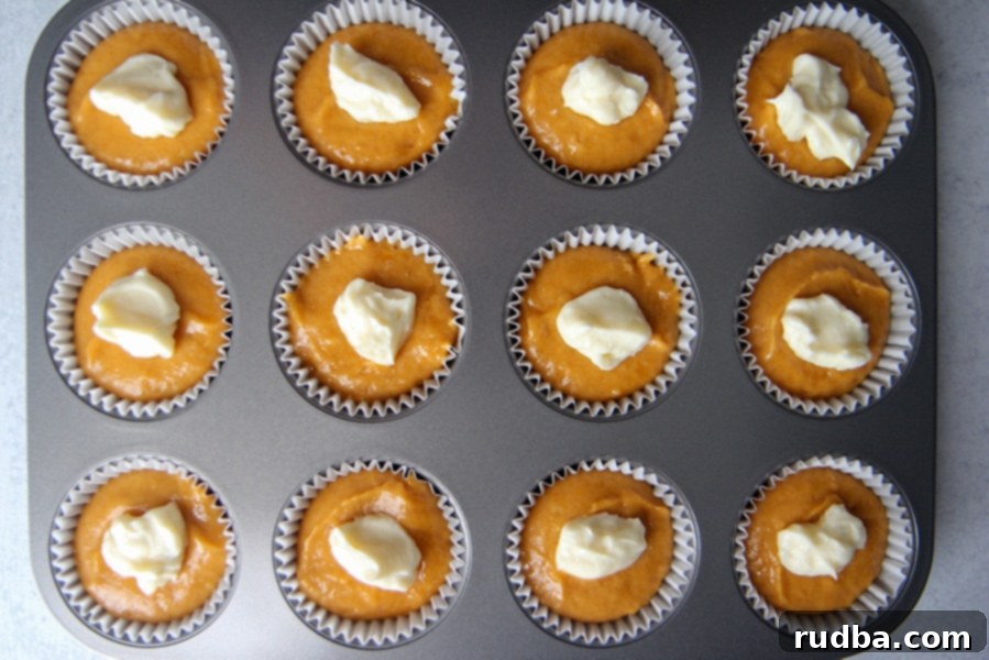 a muffin tin with 12 cupcake liners filled with muffin batter and cream cheese filling.