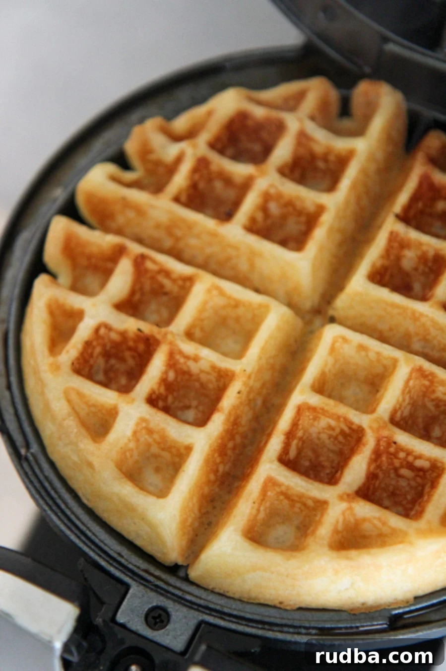 A perfectly cooked golden-brown waffle being carefully removed from a hot waffle iron using a fork or tongs.