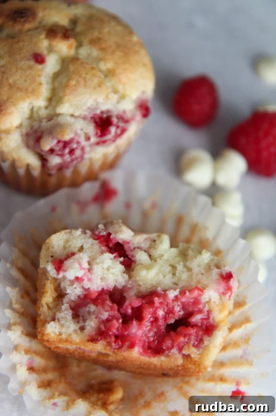A white chocolate raspberry muffin sliced in half, revealing the moist interior, red raspberries, and melted white chocolate chips.