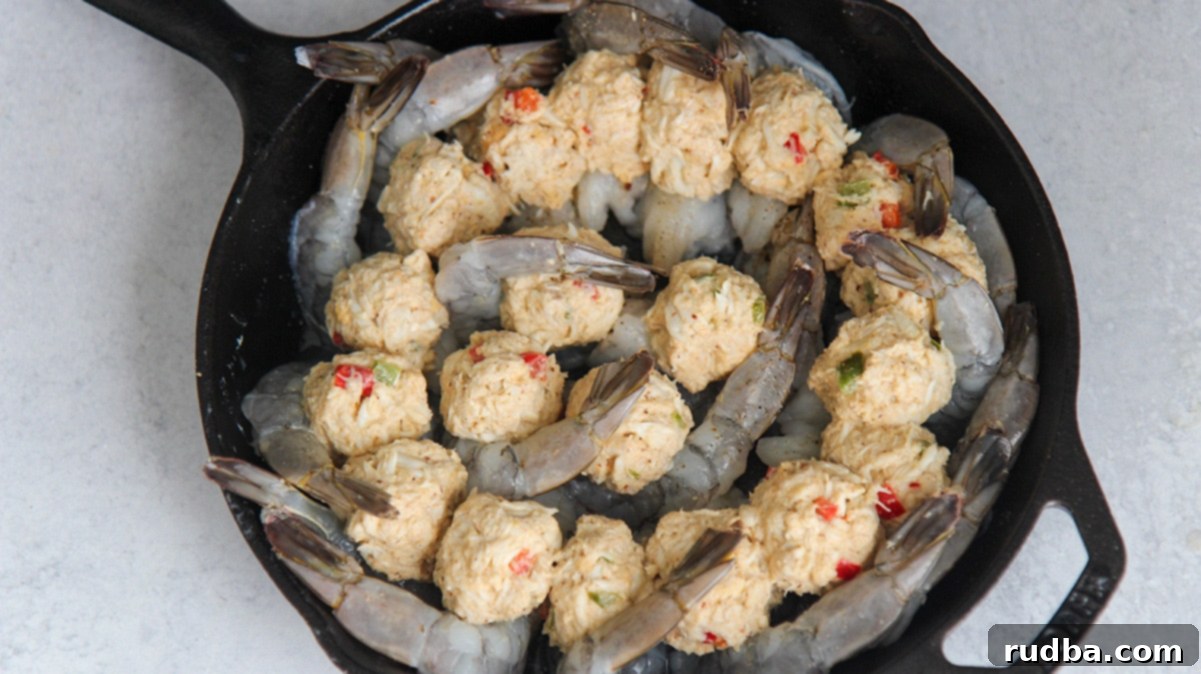 Raw jumbo shrimp butterflied and filled with rich crab stuffing, arranged in a black cast iron skillet before baking.