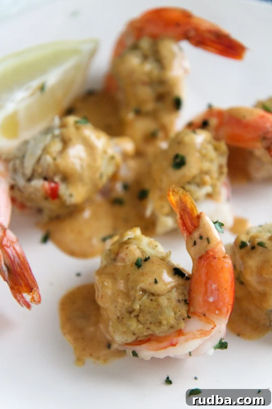 Close-up of baked crab stuffed shrimp with a generous drizzle of creamy Cajun sauce and a lemon wedge for garnish.