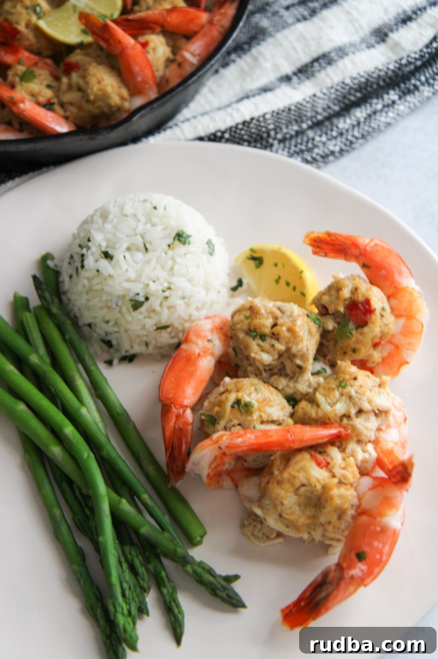 A beautifully plated dinner featuring crab stuffed shrimp, white jasmine rice, and steamed asparagus on a white plate.