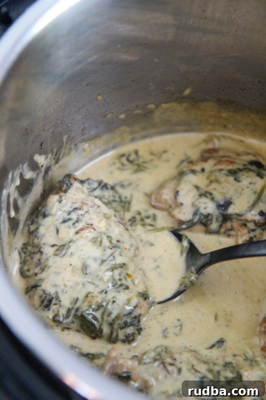 Effortless Instant Pot Tuscan Chicken 3 Tuscan chicken in the Instant Pot with a black spoon, showing the creamy sauce and spinach.