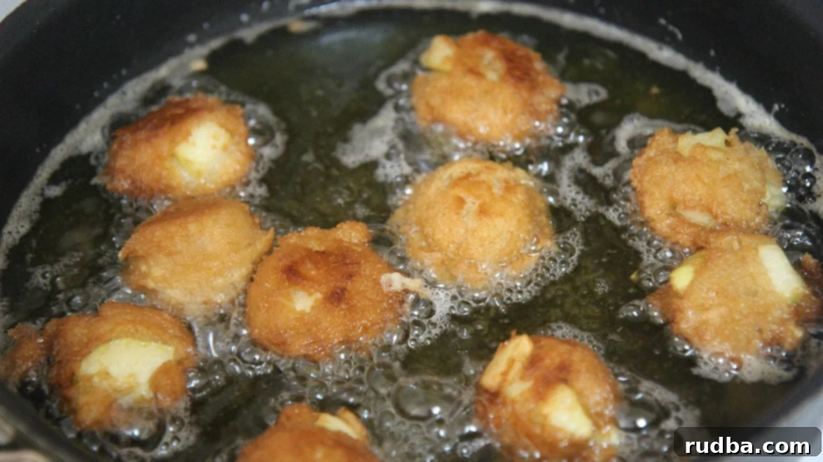 Close-up view of multiple apple fritters sizzling in hot oil within a skillet, showcasing the cooking process to achieve a perfect golden crisp.