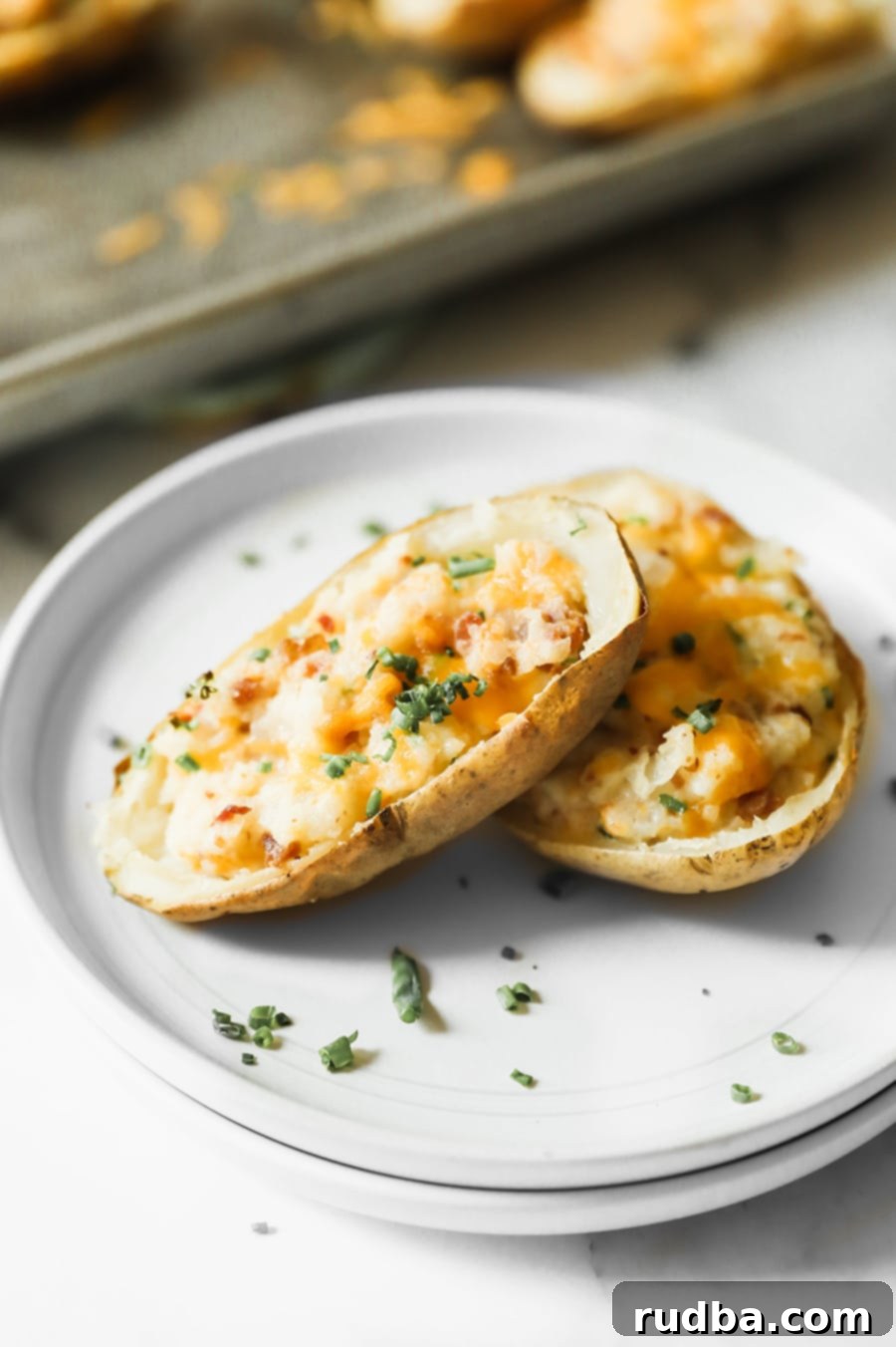 two twice baked potatoes on a white plate with green herbs on top. 
