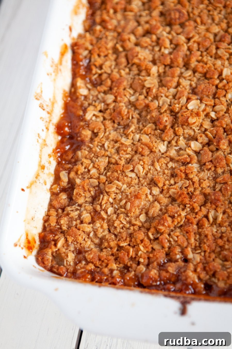 A close-up shot of a baked apple crisp, showing the golden-brown, textured oat topping and the soft, bubbling apple filling underneath.