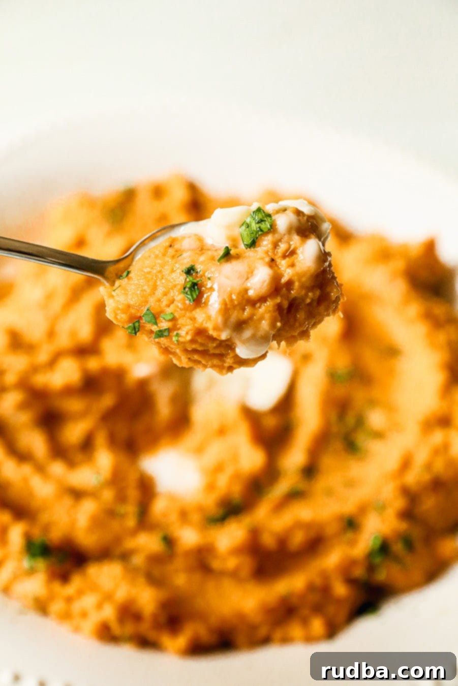 Close-up shot of a spoon scooping creamy mashed sweet potatoes with a hint of butter and spice, showcasing the smooth texture.