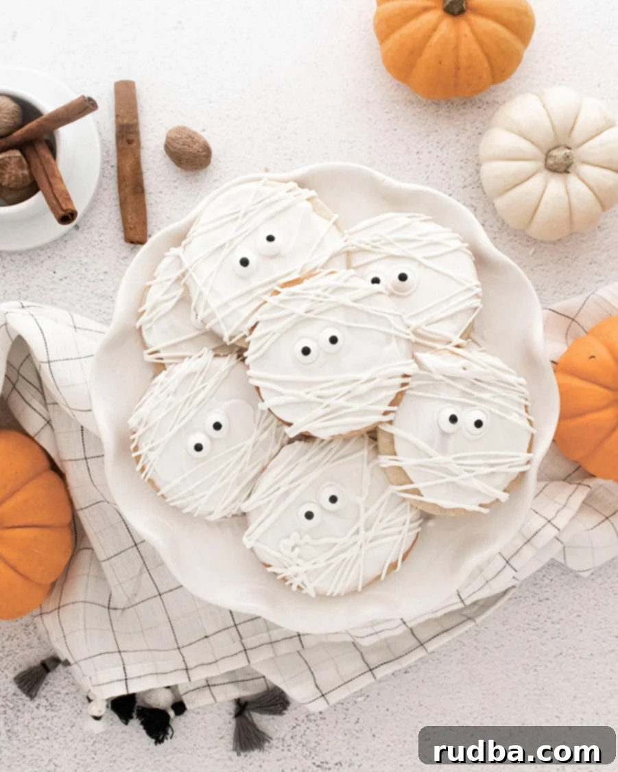 mummy cookies on a white plate with pumpkins on the side. 