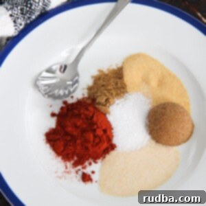 Smoky Chipotle Spice Blend 4 brown sugar and 5 spices on a white plate with a small spoon and towel on the side.