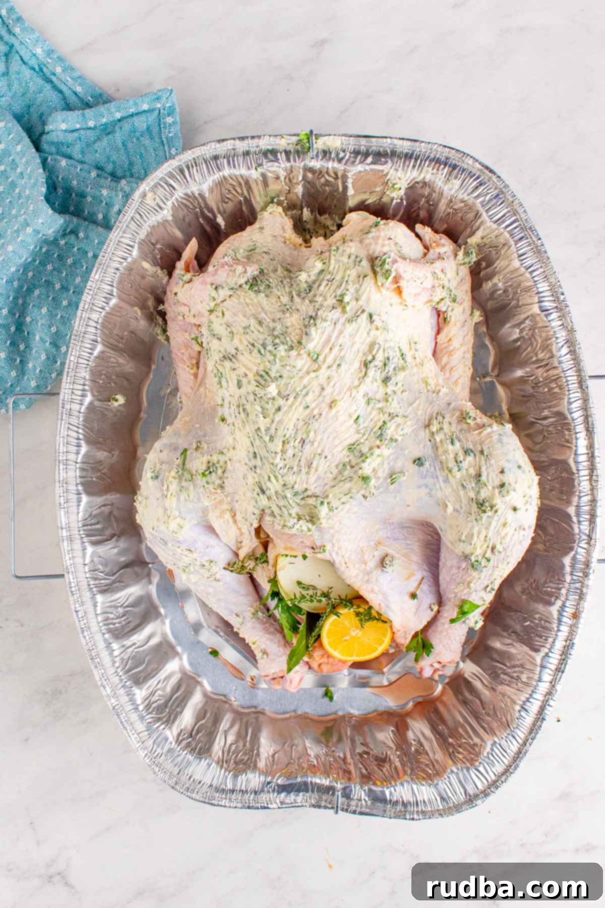 Raw turkey generously smothered with softened herb butter inside a deep baking dish, ready for roasting.