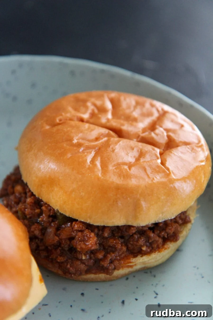 A sloppy joe up close on a blue plate, showcasing the rich, saucy meat and a melted cheese slice.