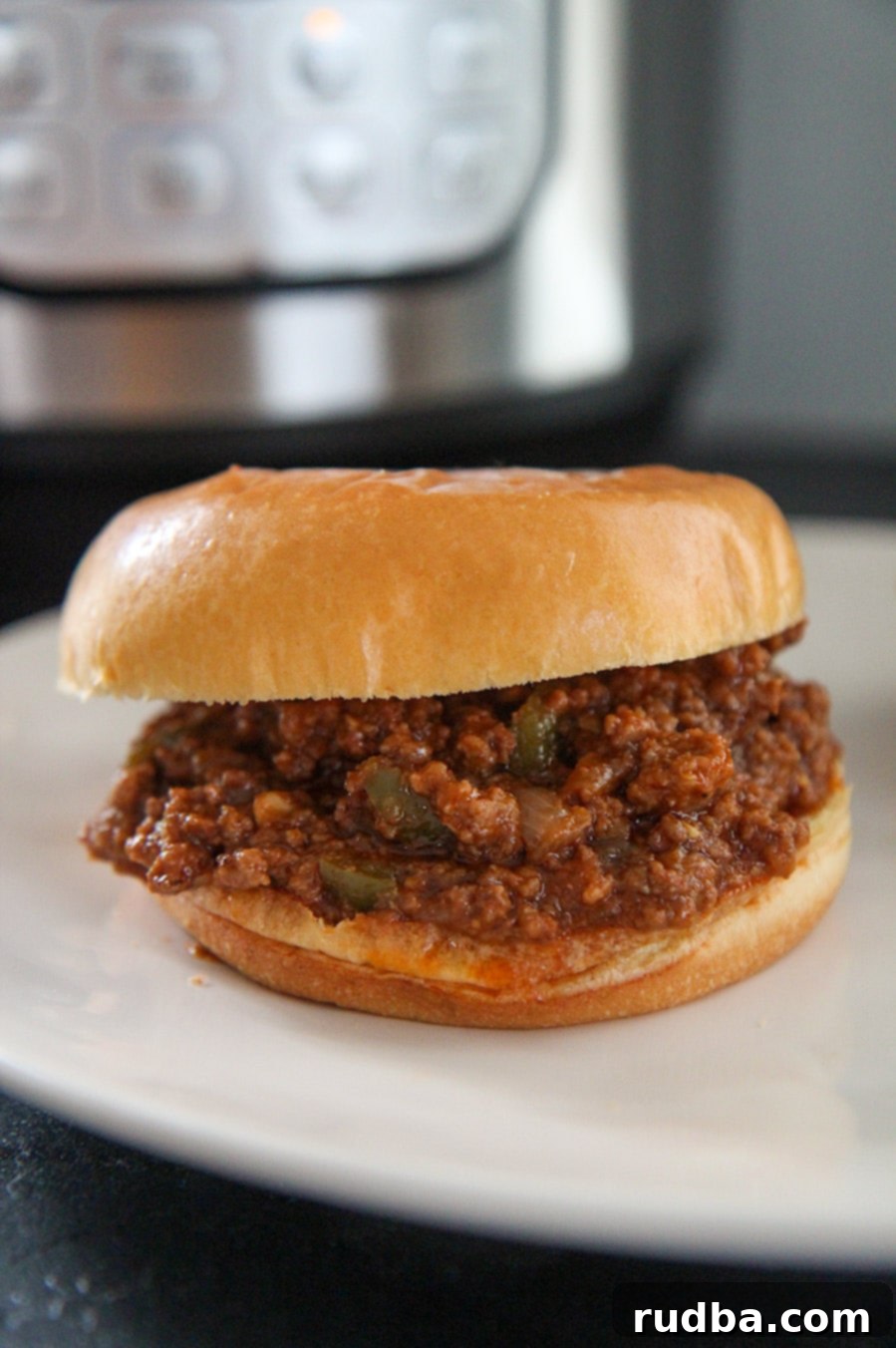 A sloppy joe sandwich with an instant pot in the background, showing the context of the recipe.