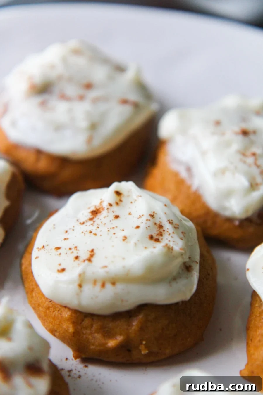 Soft pumpkin cookies generously topped with creamy cream cheese frosting and a sprinkle of cinnamon, arranged on a rustic wooden surface for a perfect fall treat.