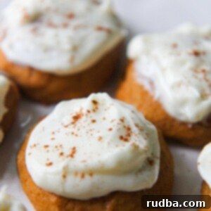 Soft and moist pumpkin cookies topped with creamy cream cheese frosting and a sprinkle of cinnamon, ready to be enjoyed.
