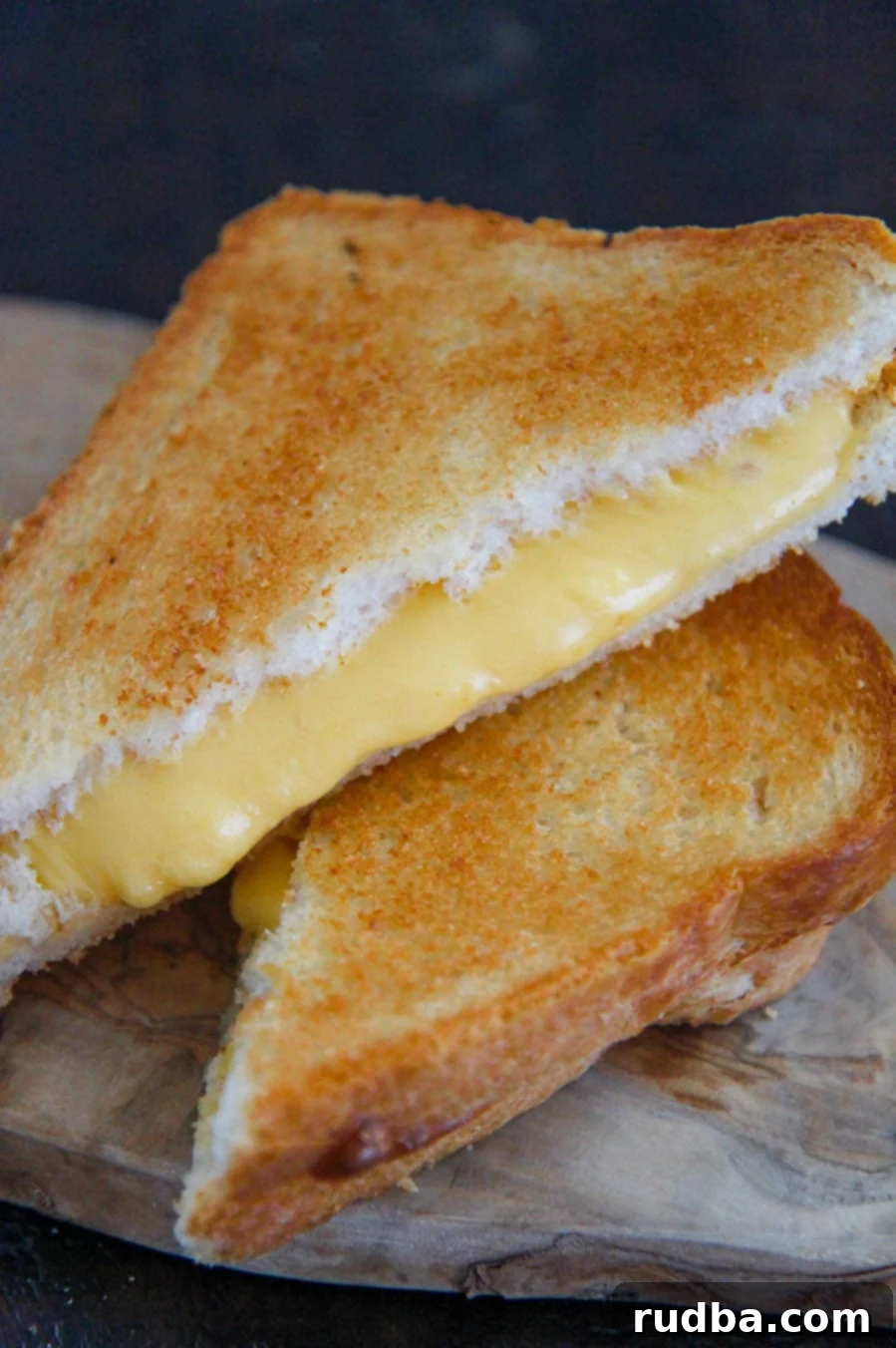 Two golden-brown air fryer grilled cheese sandwiches stacked on top of each other on a rustic wooden board, with gooey melted cheese visible.