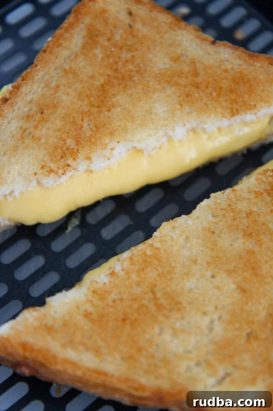 A single air fryer grilled cheese sandwich sitting in an air fryer basket, with the melted cheese oozing slightly.