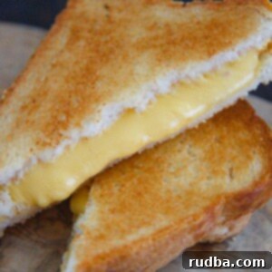 Crispy Air Fryer Grilled Cheese 4 two grilled cheese sandwiches stacked on top of each other on a wooden board.