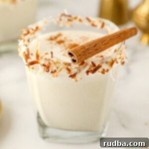 coquito in a short glass with toasted coconut on the rim and a cinnamon stick on top.