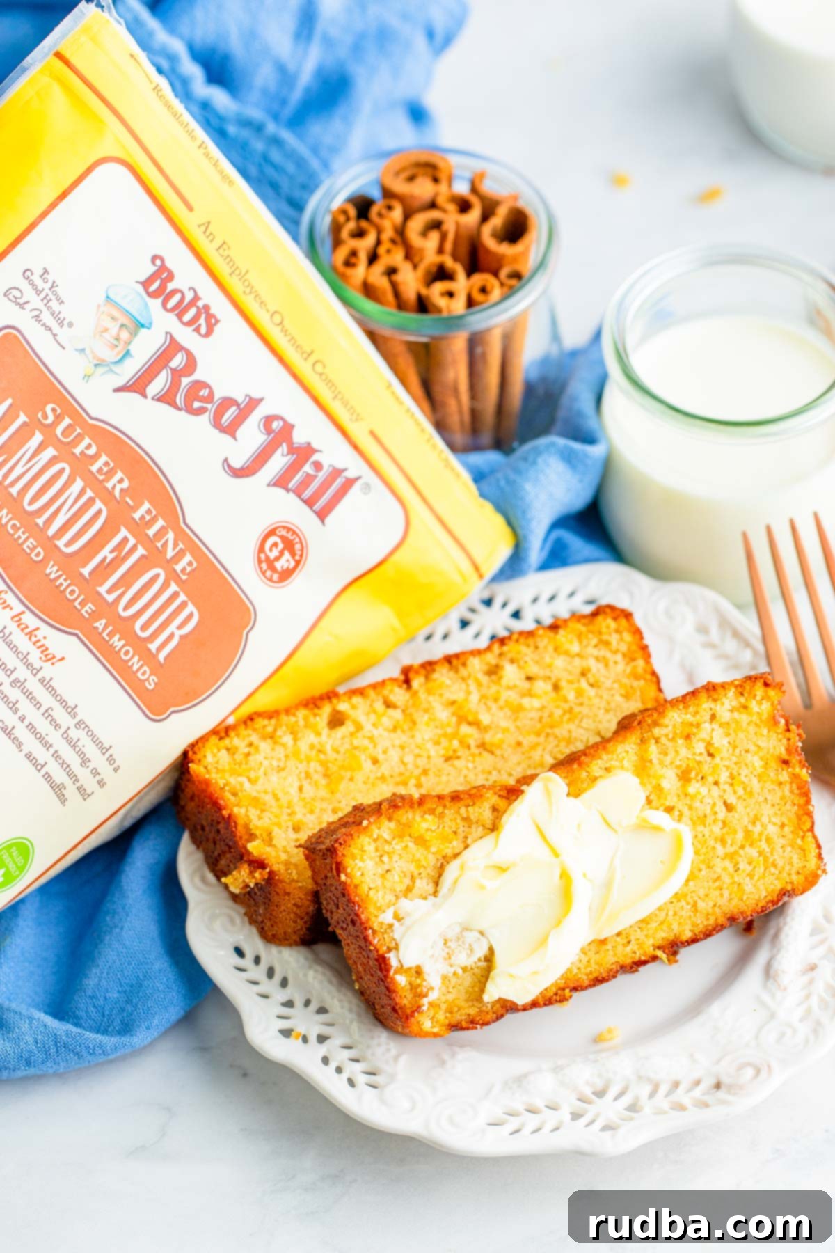 two slices of sweet potato bread with butter, a fork on the side, a glass of milk, and a package of bobs red mill almond flour. 