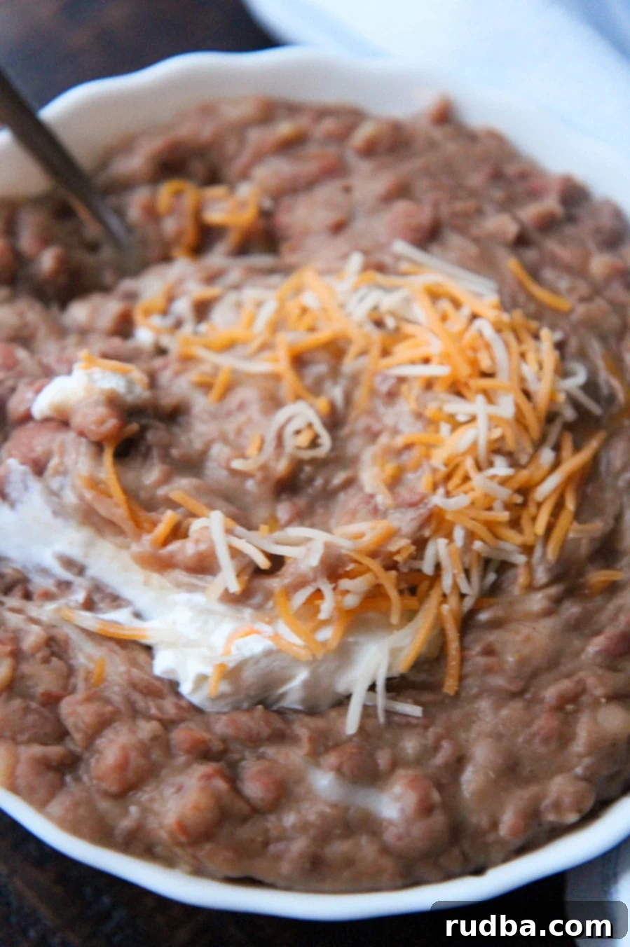refried beans with sour cream, a spoon, and cheese in a small bowl up close. 